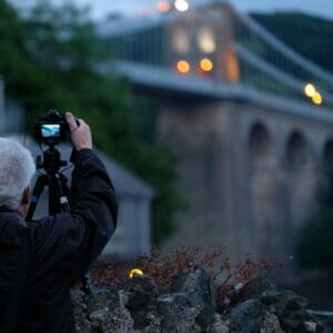 Anglesey Bridges at Night - Low-Light Photography - Square image of a Male Photographer taking a photo of the Menai Bridge on Anglesey from the Belgium Prom